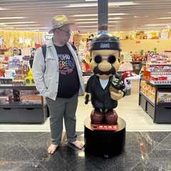 Me standing next to a Mario statue, except it's dressed in a black beanie and coat like Léon the Professional. In the statue's right hand is a handgun; it its left hand is a Piranha Plant in a ceramic pot.