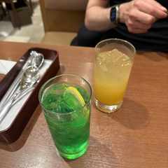A glass of green melon soda and a glass of juice.