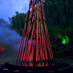 The Ember installation in Pukekura Park, with light-filled tubes arranged to resemble a camp fire. Smoke emanates from between the lights as they pulsate between off and glowing red to resemble burning wood.