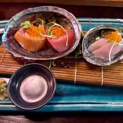 Salmon, tuna, and white fish sashimi served on pāua shells, themselves on a blue platter with ginger and wasabi.