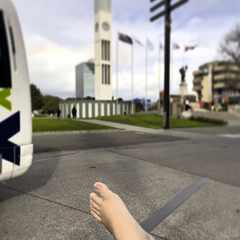 A photo of the Square in Palmerston North. In the foreground, the top of my left bare foot; in the background, the clock tower that stands at the centre of the Square.