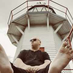 Me sitting on the ground in front of the Portland Island lighthouse in Wairoa. Similar to the first picture in this article, my phone camera is on the ground and pointing at me with a clear view of the soles of my feet. In this one, both feet are visible instead of just one and I am looking at something out of frame.