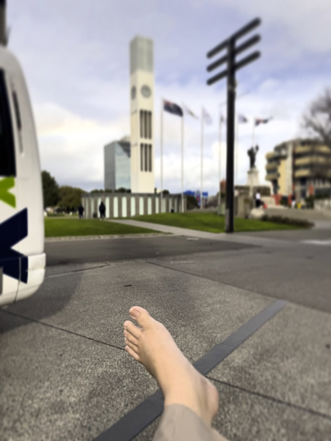 A photo of the Square in Palmerston North. In the foreground, the top of my left bare foot; in the background, the clock tower that stands at the centre of the Square.