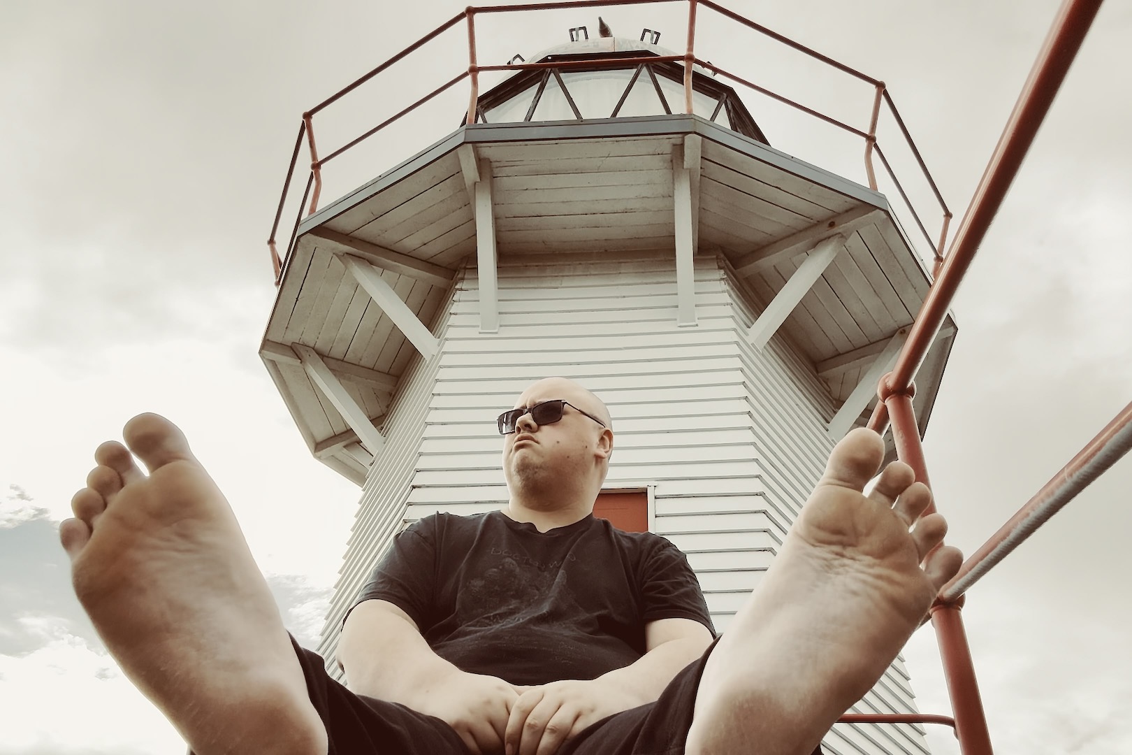 Me sitting on the ground in front of the Portland Island lighthouse in Wairoa. Similar to the first picture in this article, my phone camera is on the ground and pointing at me with a clear view of the soles of my feet. In this one, both feet are visible instead of just one and I am looking at something out of frame.